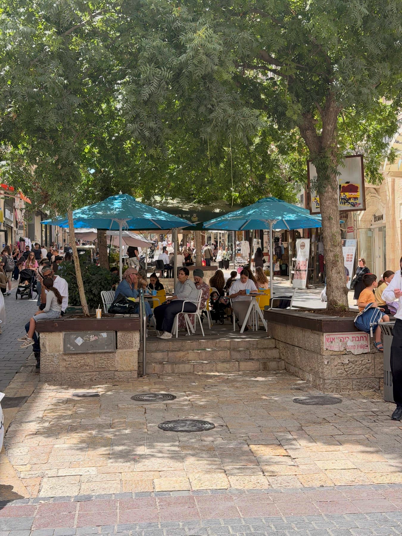 People sitting at shaded café tables under the trees on Ben Yehuda Street, Jerusalem